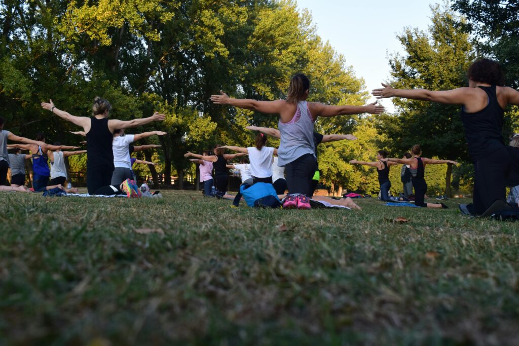 pexels-photo-1472887-1472887 Group of adults practicing yoga outdoors in a park surrounded by trees.